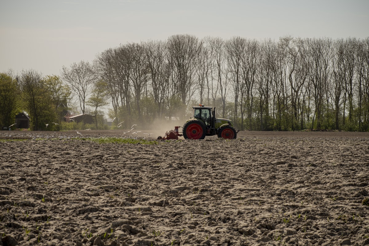 Tractor verde y naranja arando un campo de tierra marrón